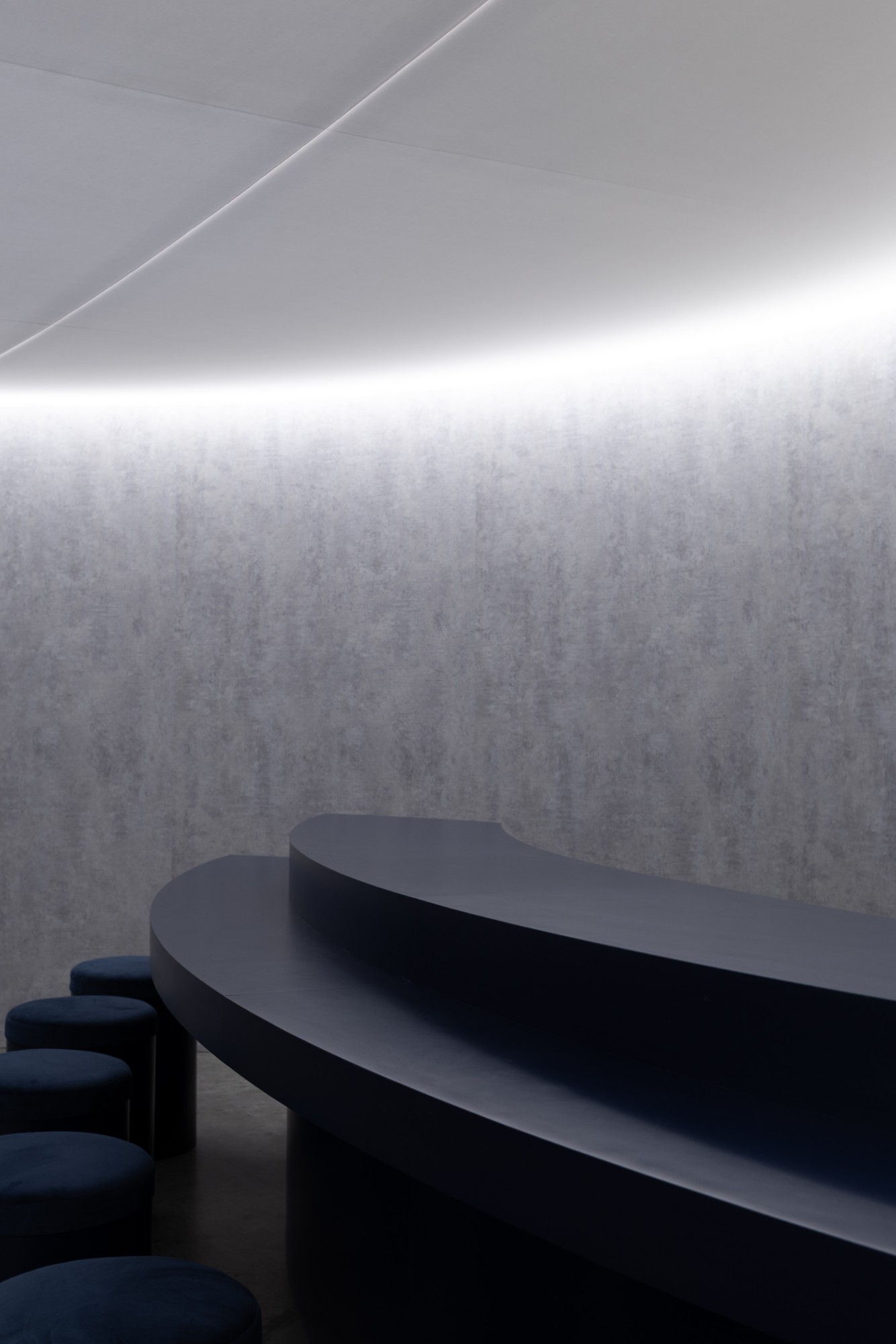 The curved navy sushi bar and velvet stools under a ring of light